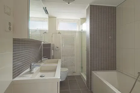 Een neutrale badkamer met ligbad, douchewand en dubbele wastafel